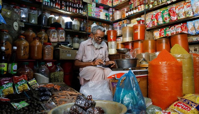 A shopkeeper uses a calculator while selling spices and grocery items along a shop in Karachi. — Reuters/File