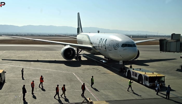 Ground staff stand next to a Pakistan International Airline (PIA) aircraft ahead of its takeoff for Paris at the Islamabad International Airport on January 10, 2025. — APP