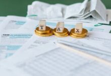 A representational image of a table where coins and cubes with tax letters written on them are placed on the papers. — Pexels
